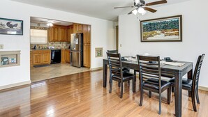 Un coin repas avec une table et des chaises, un ventilateur de plafond et une cuisine en arrière-plan.