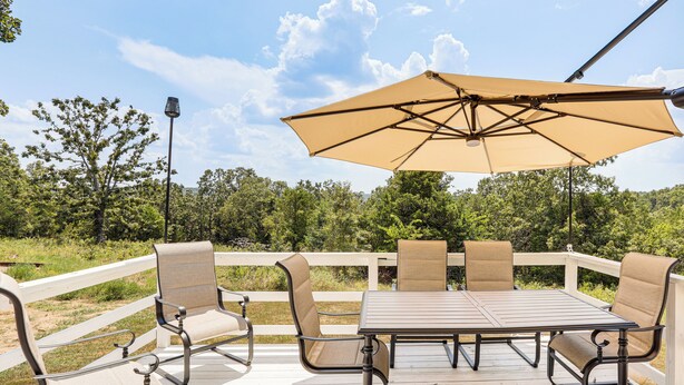 Une terrasse dotée d’une table et de chaises, entourée d’une balustrade blanche, et offrant une vue sur un paysage naturel.