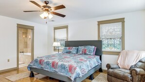 Une chambre à coucher comprenant un lit, une chaise, un ventilateur de plafond et une fenêtre avec des stores.