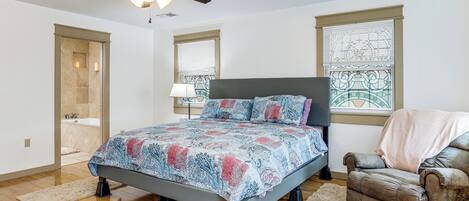 Ein Schlafzimmer mit Bett, Stuhl, Deckenventilator und einem Fenster mit Jalousien.