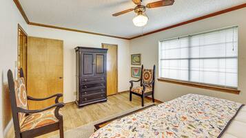Un dormitorio con una cama, una silla, un aparador y un ventilador de techo.