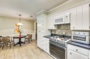 A kitchen with white cabinets, a microwave, a stove, and a dining area with a table and chairs.