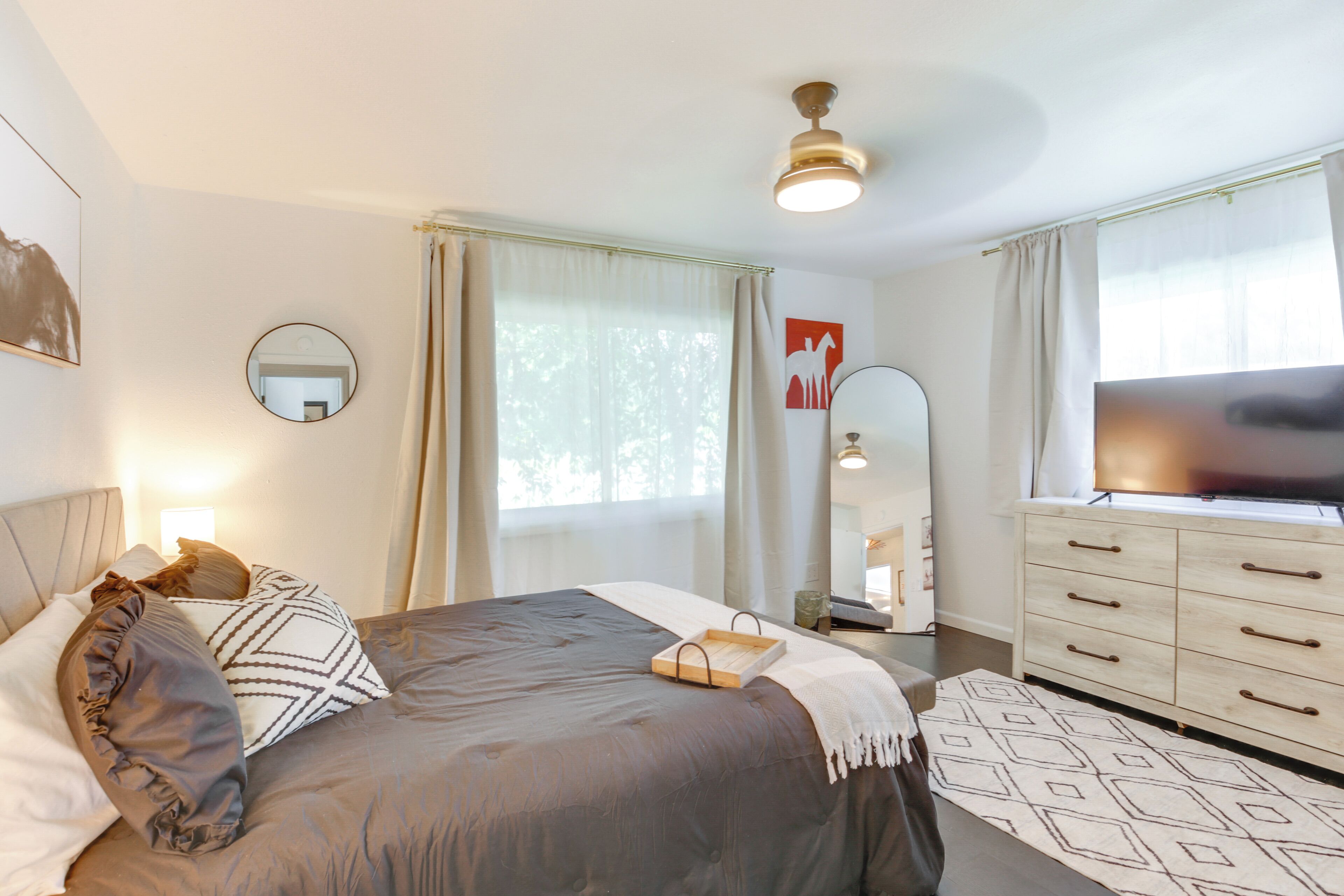 A neatly arranged bedroom with a bed, bedside table, dresser, and a television.