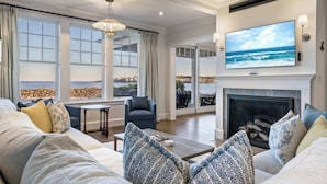 A modern living room with a large TV, a fireplace, and a view of the ocean. - Oceanfront Home w/ Semi-Private Beach • Sleeps 12 (York)