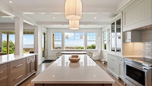 A spacious kitchen with a large island, modern appliances, and large windows offering views of the outdoors. - Oceanfront Home w/ Semi-Private Beach • Sleeps 12 (York)