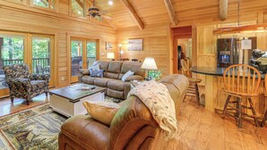 A spacious living room with a large couch, a coffee table, and a dining area with wooden chairs. - Luxe Mountain Escape w/ Hot Tub & Gym Near Boone! (Zionville)