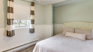 A bedroom with a bed, a window with curtains, a radiator, and a ceiling fan.
