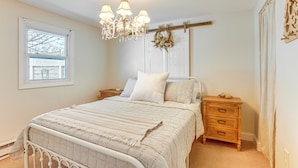 A bedroom with a bed, a wooden nightstand, a dresser, a chandelier, a window, and a door.