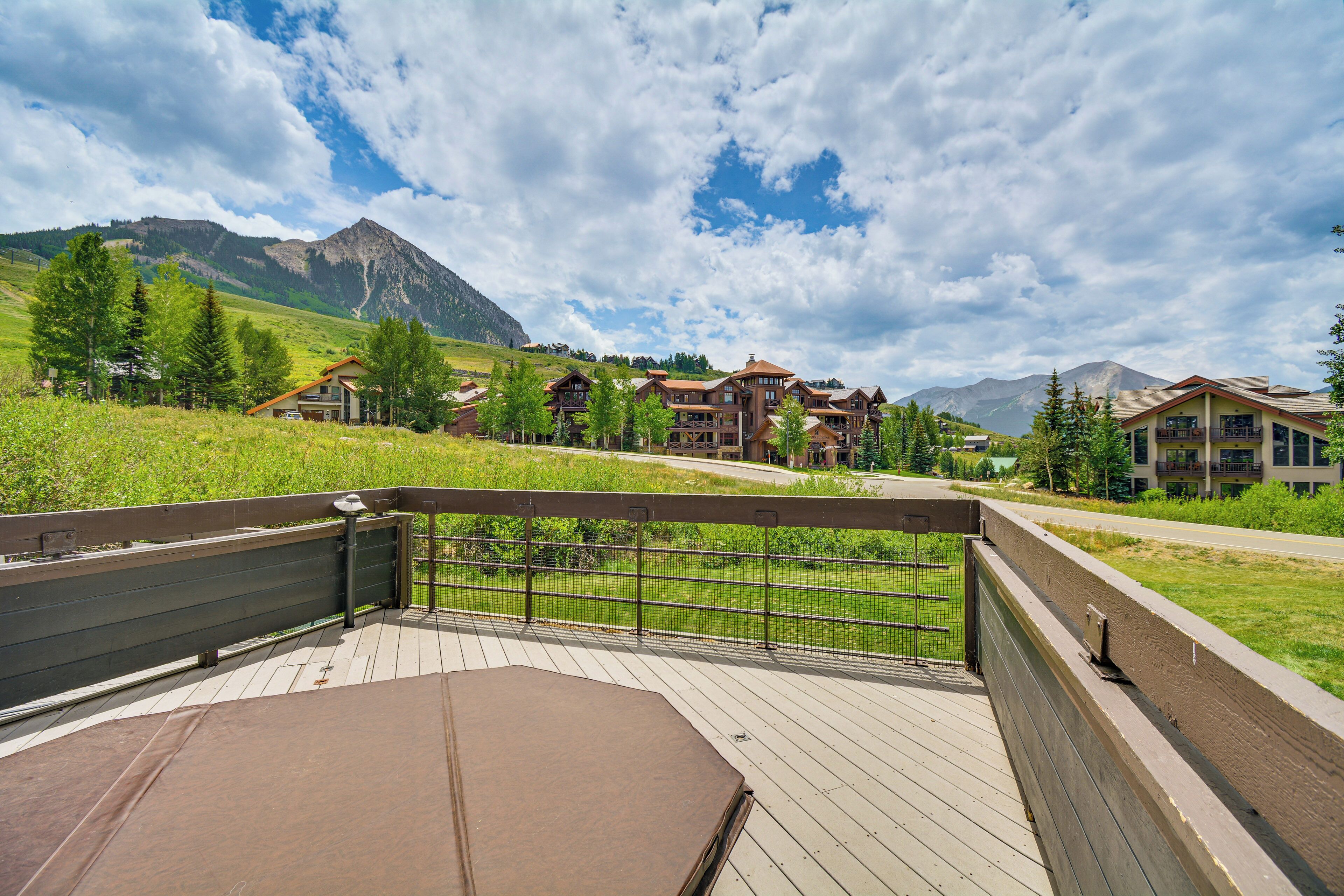 A wooden deck with a metal railing overlooking a mountain resort with multiple buildings.