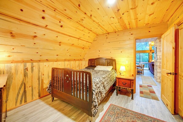 A wooden cabin bedroom with a bed, nightstand, and a view of the outside. - Explore Mt St Helens: A-frame Chalet w/ Deck! (Ariel)