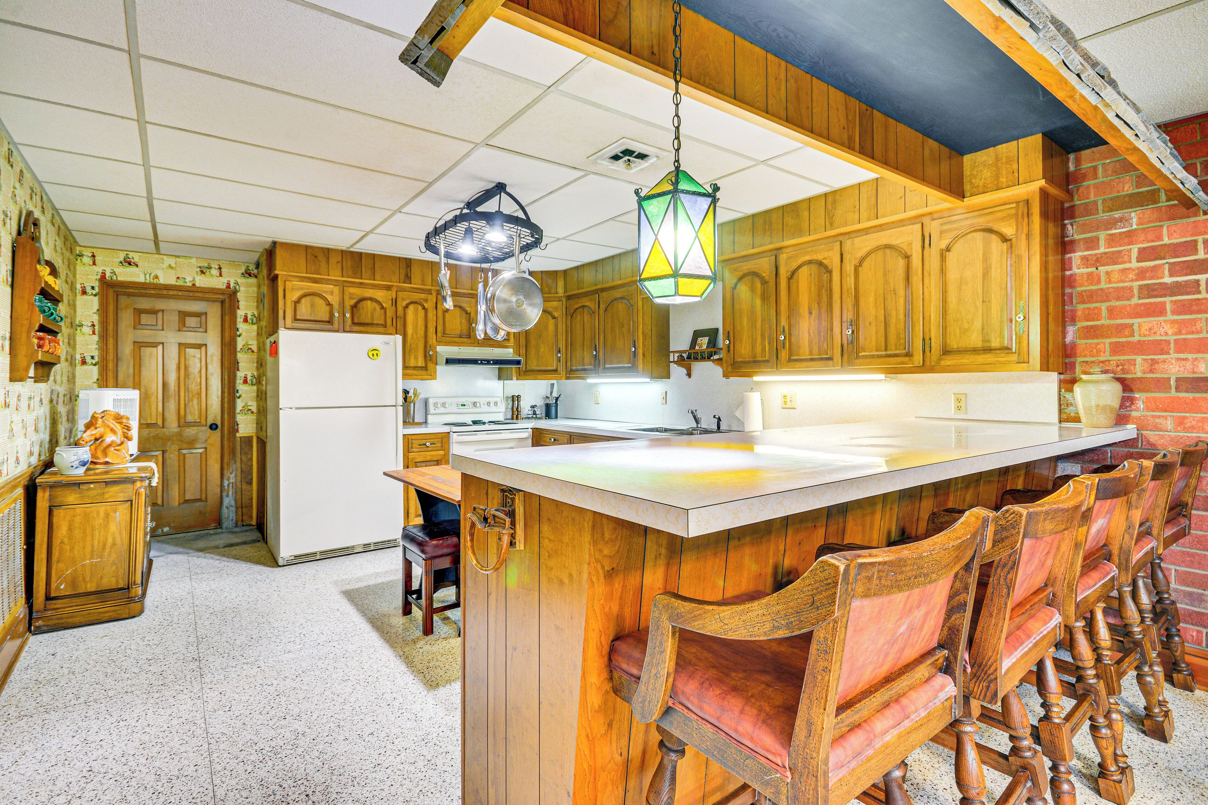 Une cuisine avec des meubles en bois, un grand îlot central doté de tabourets, un réfrigérateur et des luminaires suspendus.