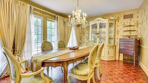 Una sala de dinar formal amb una taula de fusta, cadires ornamentades, un penjallum i un aparador de vidre amb objectes decoratius.