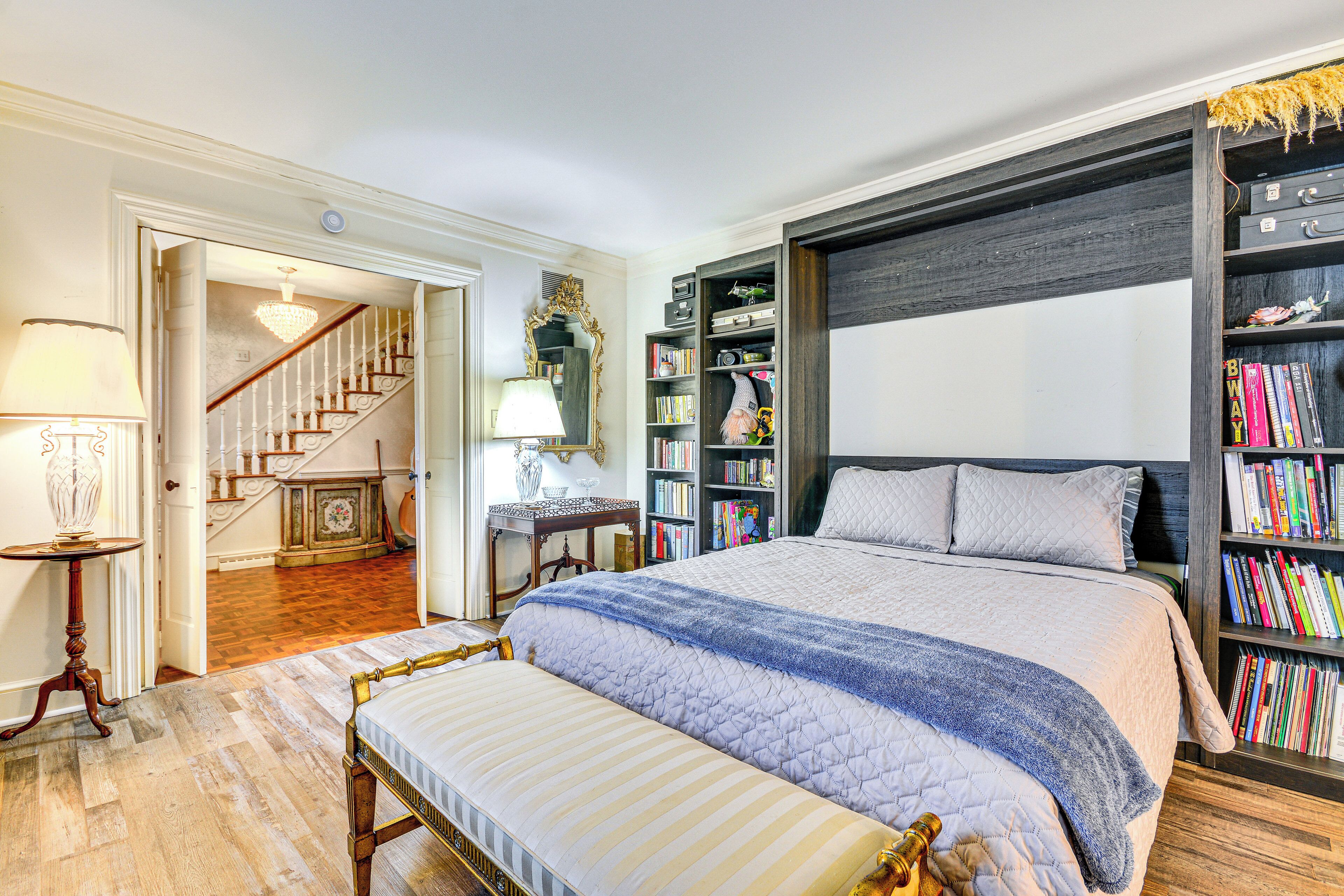 Een slaapkamer met een groot bed, een boekenkast, een bureau en een trap naar een andere kamer.