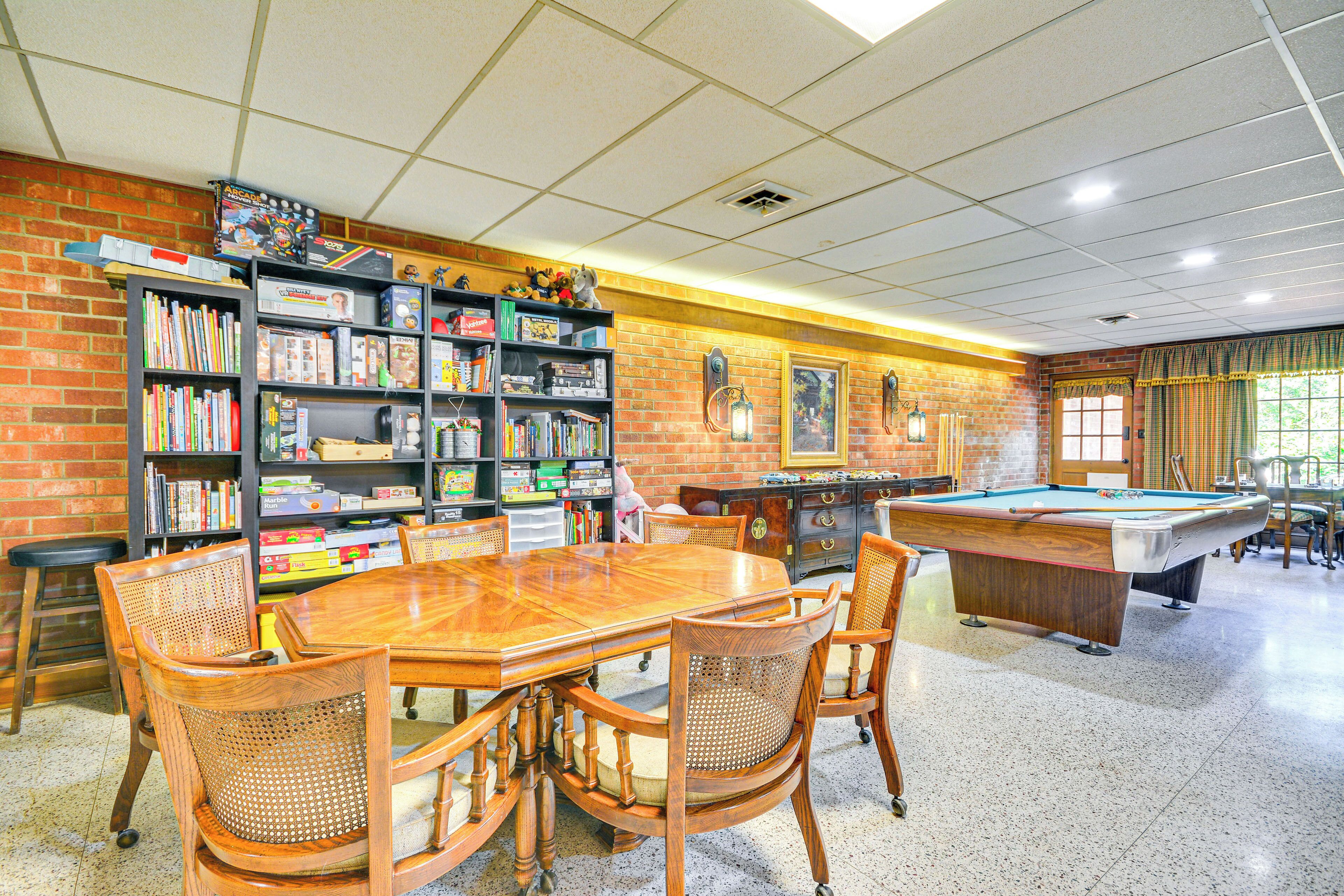 A billiards room with a pool table, wooden chairs, and a bookshelf filled with books and games.