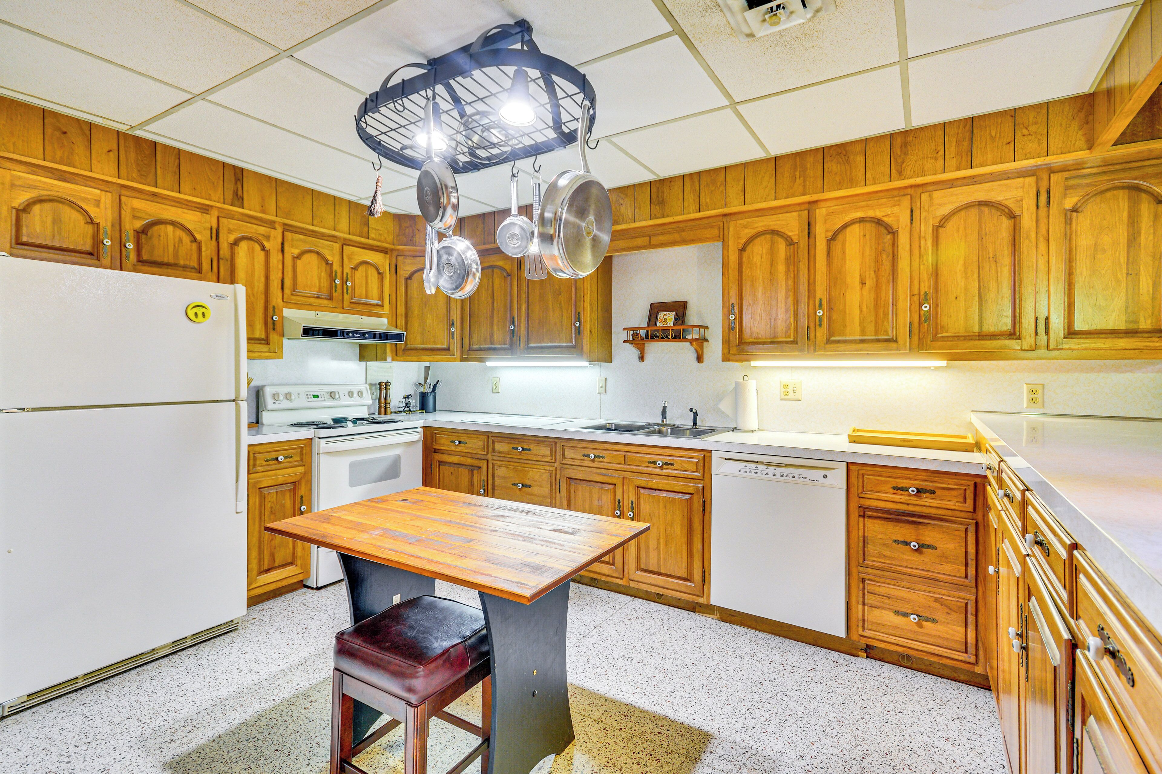 Eine Küche mit Holzschnitzschränken, einem weißen Kühlschrank, einem Herd und einem Holzessttisch mit einer Bank.