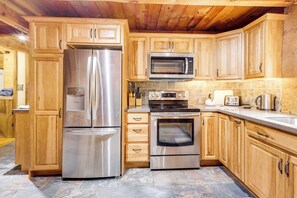 Eine moderne Küche mit Edelstahlgeräten, Holzschränken und Fliesenboden aus Stein.
