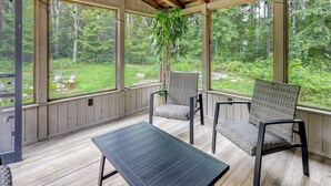 A covered porch with wooden flooring, two wicker chairs, a table, and large windows offering a view of a green landscape. - 7 Mi to Glens Falls: Peaceful Retreat w/ Game Room (Hudson Falls)
