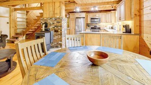 A wooden interior with a dining table, chairs, a wooden bowl, a brick fireplace, kitchen appliances, and a staircase. - 7 Mi to Glens Falls: Peaceful Retreat w/ Game Room (Hudson Falls)