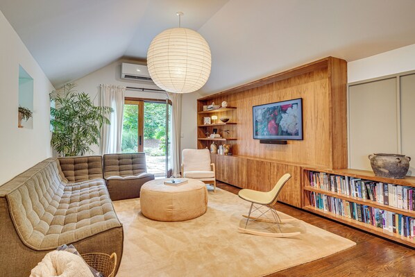 A modern living room with a sectional sofa, a round ottoman, a rocking chair, a bookshelf, and a television mounted on a wooden wall. - 15 Mi to Long Island Sound: Bedford Winter Retreat (Bedford)
