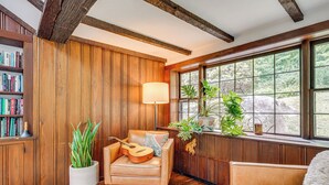 A cozy room with wooden walls, a bookshelf, a leather armchair, a guitar, and a window with a view of greenery. - 15 Mi to Long Island Sound: Bedford Winter Retreat (Bedford)
