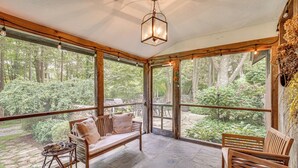 A cozy, enclosed porch with wooden furniture, large windows offering a view of a lush garden. - 15 Mi to Long Island Sound: Bedford Winter Retreat (Bedford)