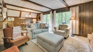 A cozy living room with wooden beams, a sofa, a chair, and a dining table. - Cabin Near Lake w/ Deck, Fire Pit & Grill! (Elmira)