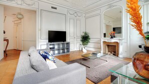 Een woonkamer met een bank, televisie, open haard en decoratieve spiegel.