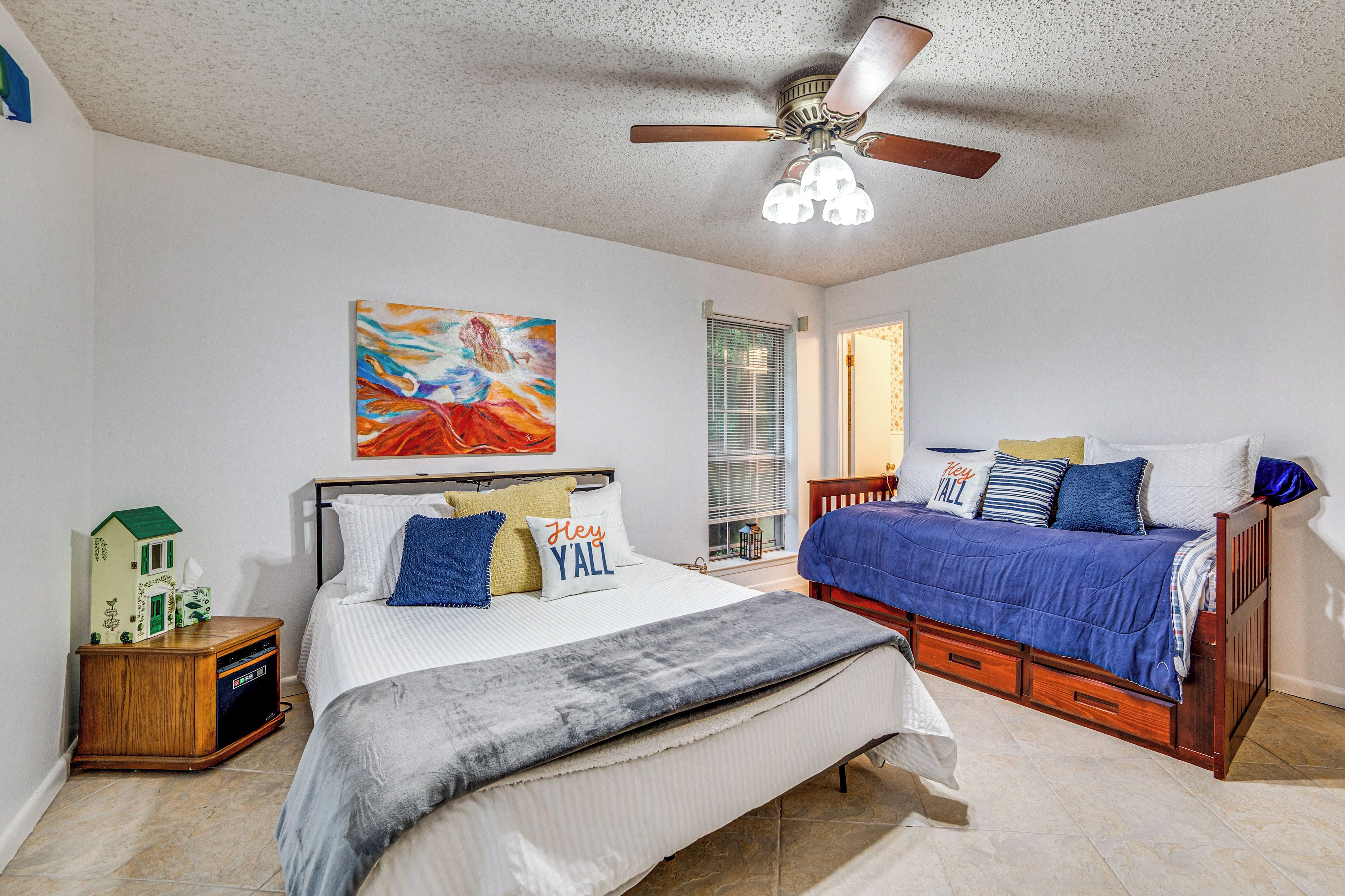 A bedroom with two beds, a ceiling fan, and a painting on the wall.