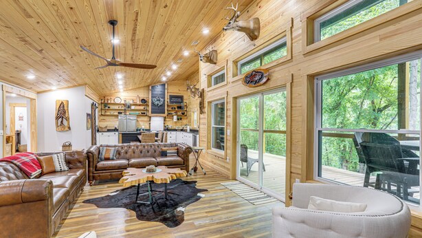 A spacious living area with leather sofas, a coffee table, and a large window offering a view of the outdoors. - Relax on the River: Modern Mountain View Escape! (Mountain View)