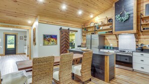 A modern kitchen with a central island, built-in appliances, and a dining area with wicker chairs. - Relax on the River: Modern Mountain View Escape! (Mountain View)