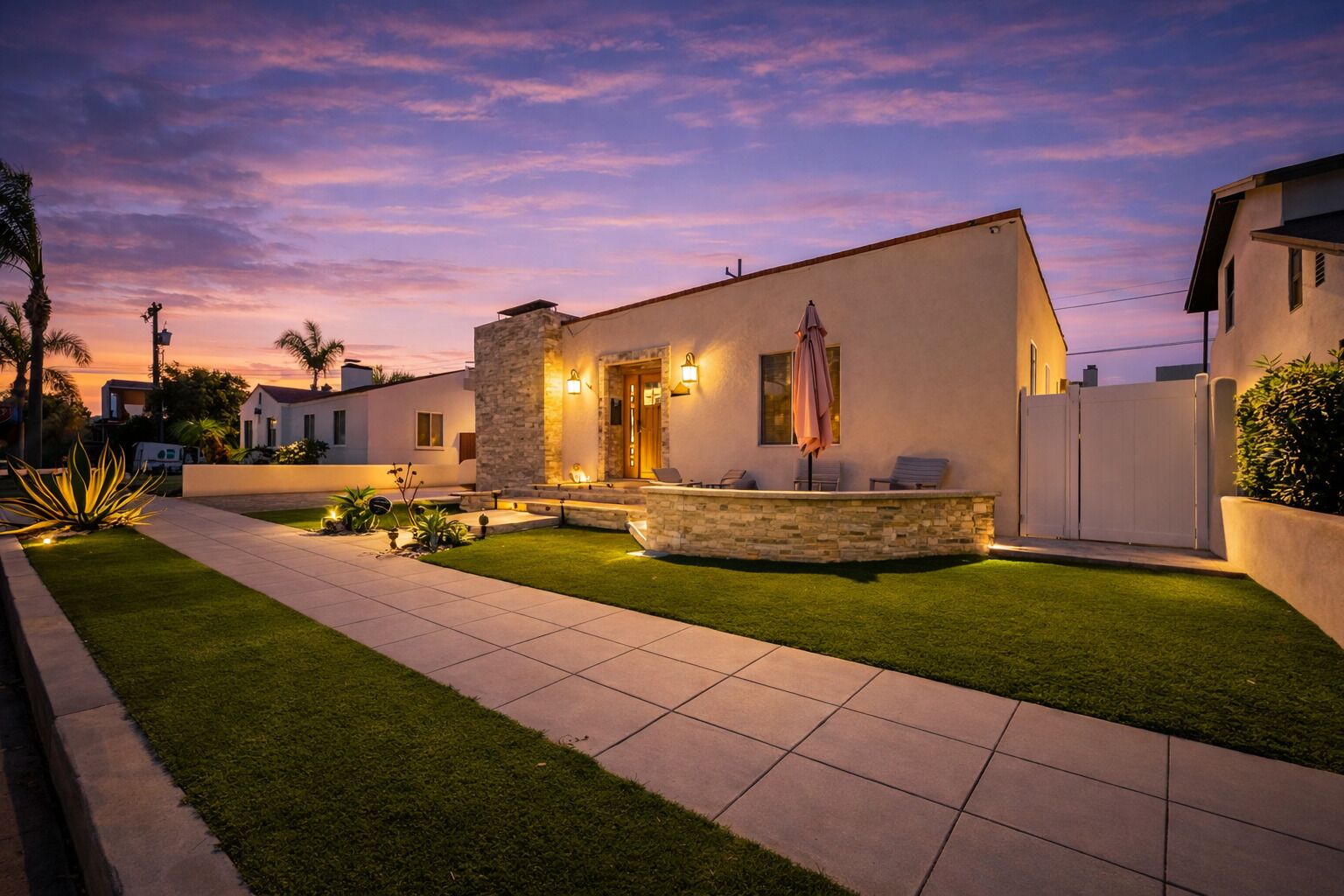 Una casa moderna con fachada de piedra, césped cuidado y zona de estar al aire libre.
