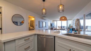 Een moderne keuken met witte kasten, een roestvrijstalen vaatwasser en hanglampen.