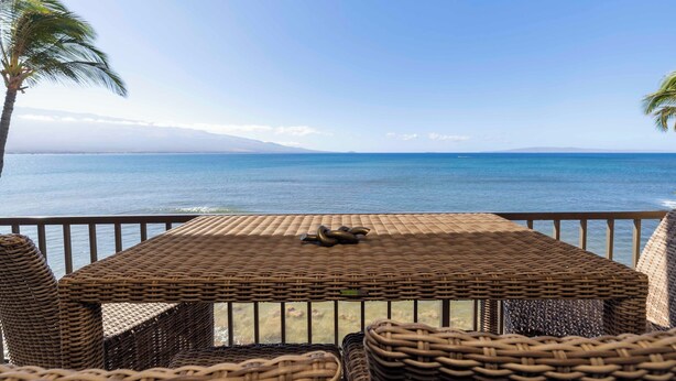Een balkon met rieten tafeltje en stoelen en uitzicht op de oceaan.