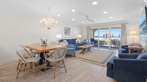 A spacious living area with a dining table, chairs, sofas, and a view of the beach through large windows.