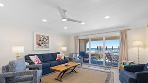 A modern living room with a sofa, armchairs, a coffee table, and a view of the ocean through large sliding doors.