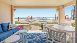A balcony with a view of the beach, a pool, and lounge chairs.