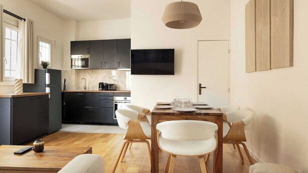 A modern kitchen with dark cabinets, a built-in oven, and a flat-screen TV. - Amazing Apartment - 2br/6p - Nation (Paris)