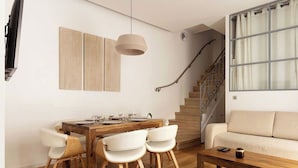 A modern living room with a wooden dining table, white chairs, a sofa, and a staircase. - Amazing Apartment - 2br/6p - Nation (Paris)