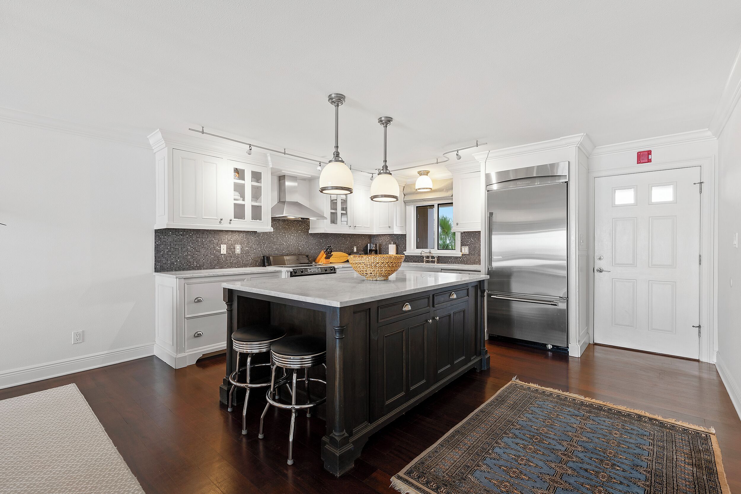 A modern kitchen with dark cabinetry, a large island, stainless steel appliances, and pendant lighting.