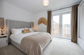 A bedroom with a large bed, a bedside table, a wall-mounted fan, and a view of the outside through a sliding door.