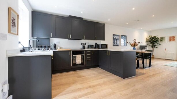 A modern kitchen with dark cabinetry, a central island, and a dining area with a table and chairs.