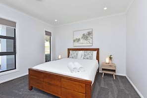 Une chambre à coucher avec un lit en bois, une table de chevet avec une lampe, une fenêtre et un tableau accroché au mur.