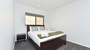 A bedroom with a bed, a nightstand, a window with a view of a brick wall, and a bedside lamp.
