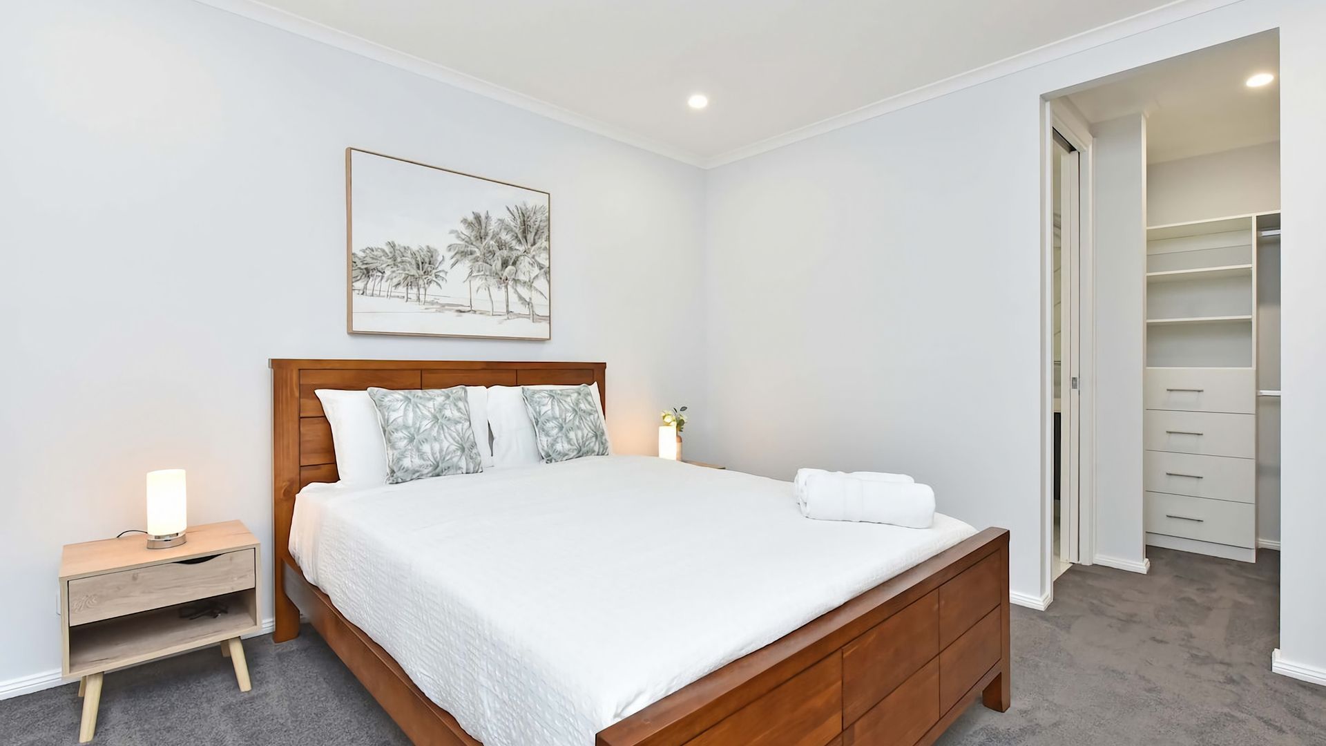 A bedroom with a wooden bed, a bedside table with a lamp, a framed picture on the wall, and a walk-in closet.