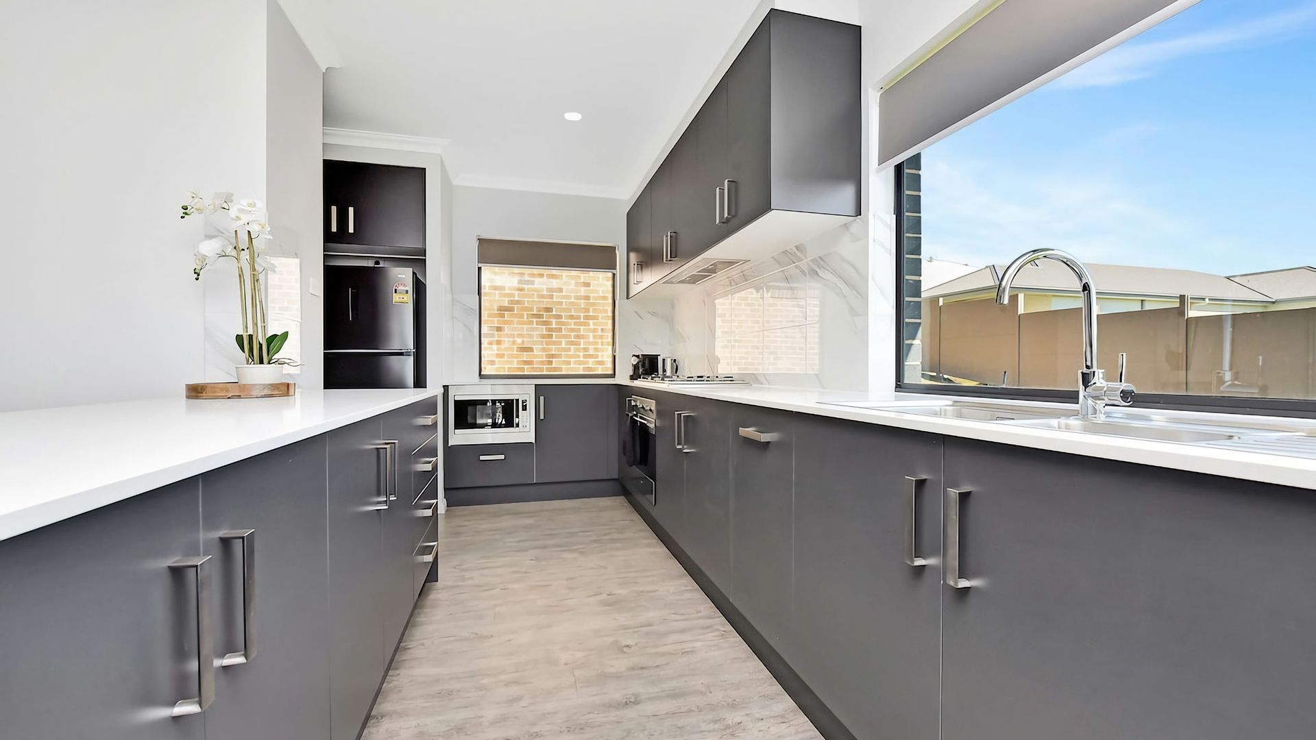 A modern kitchen with grey cabinetry, a white countertop, and a view of the outside.