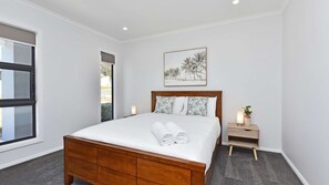 A bedroom with a wooden bed, white bedding, a nightstand with a candle, and a framed picture on the wall.
