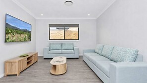 A modern living room with a light blue sofa, a wooden coffee table, and a TV on the wall. - Huntlee Heights | {et Friendly with Fire Pit (North Rothbury)