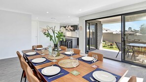 A dining area with a wooden table set for six, a vase with flowers, and a view of the backyard through a glass door. - Huntlee Heights | {et Friendly with Fire Pit (North Rothbury)
