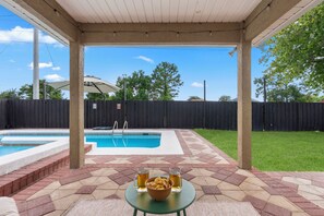 A covered patio with a pool, a table with drinks, and a fenced backyard. - NEW! The Flip Flop Fortress (Panama City Beach)
