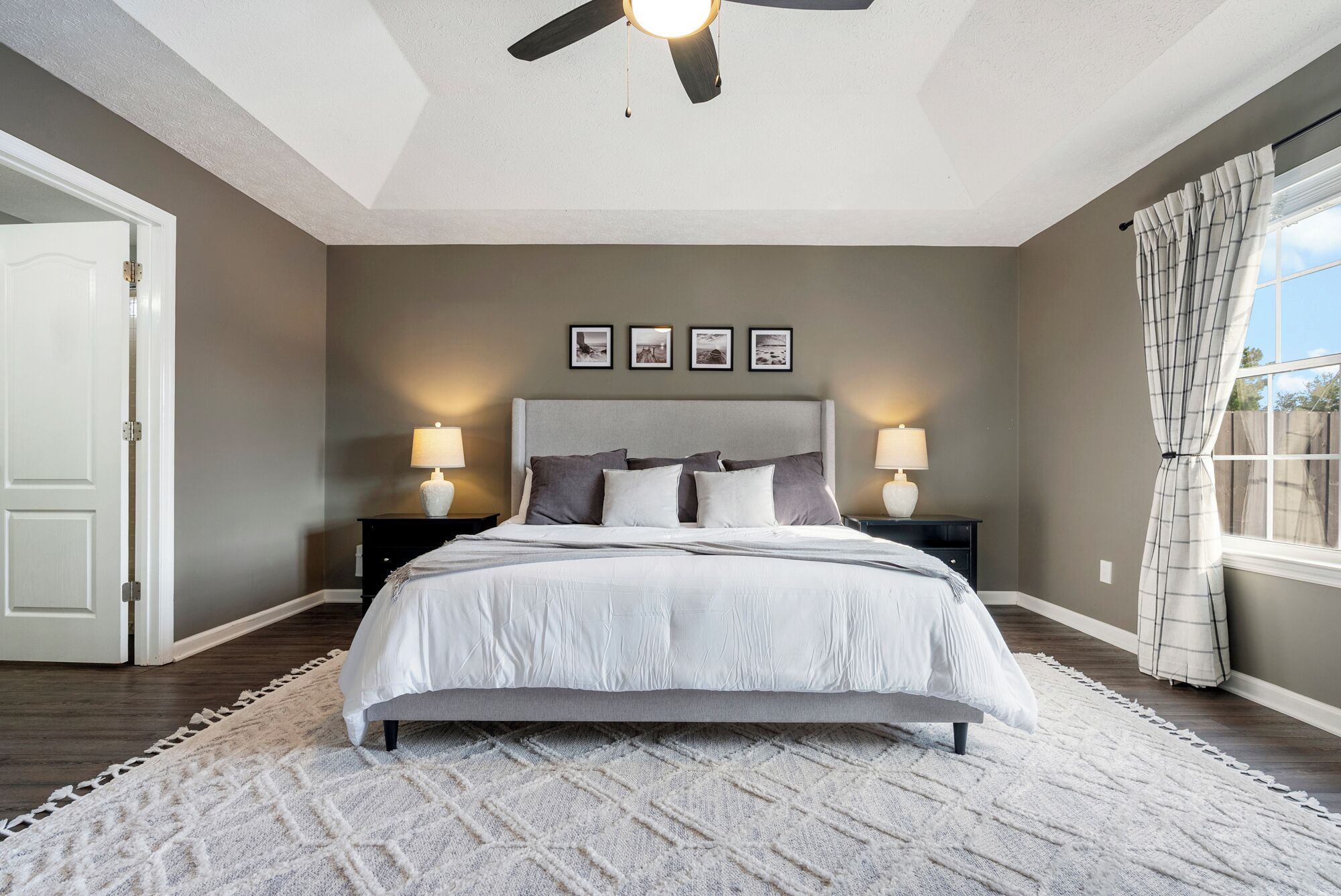 A bedroom with a bed, two bedside tables, a ceiling fan, and a window with curtains.